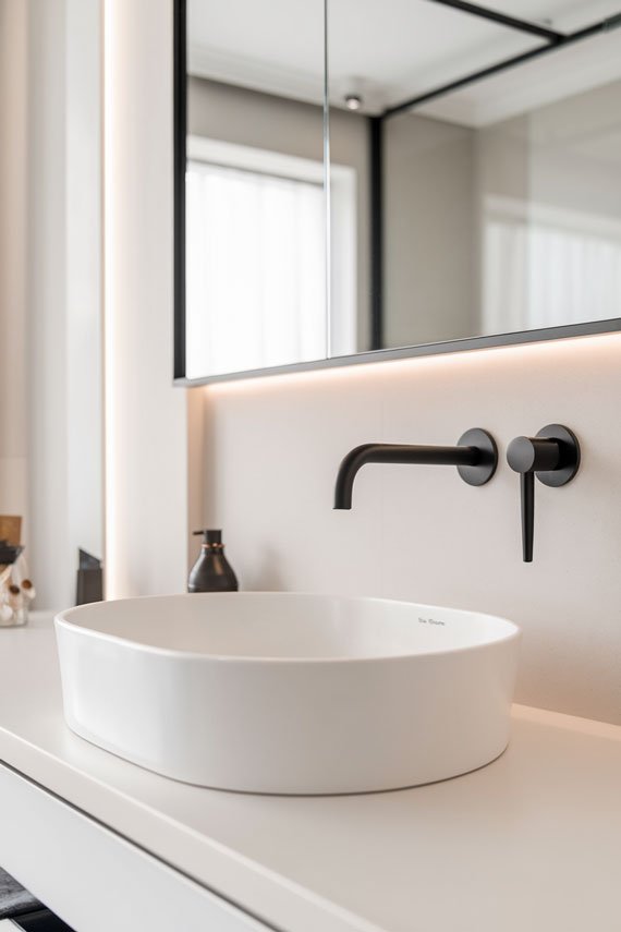 Matte black wall-mounted faucet above vessel sink.